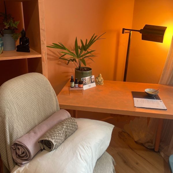 desk, with a plant, and lamp, with a chair covered in neatly rolled massage towels.